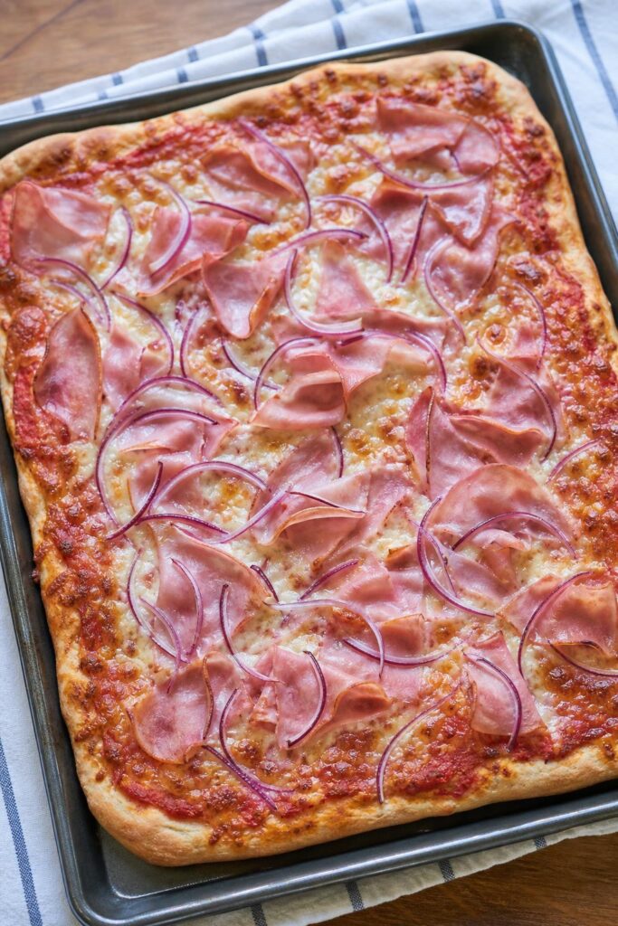 Homemade ham pizza on a tray with cheese and tomato base